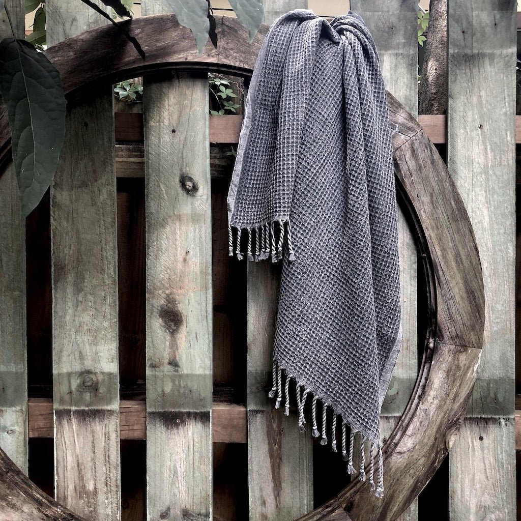 Gray woven blanket with fringes draped over a wooden fence